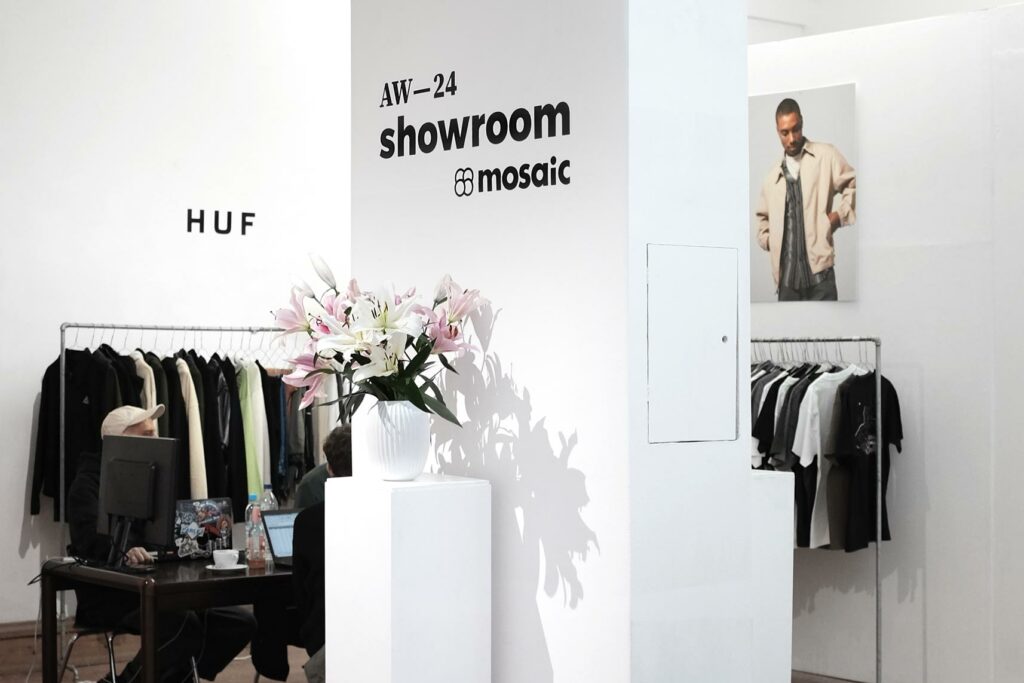 Photography of Mosaic's Autumn Winter 2024 showroom in Berlin. The image shows a brand corner dedicated to the streetwear label HUF, as well as a bouquet of lilies and a black vinyl sticker on one of the many white walls, saying »AW—24 showroom« above the Mosaic logo.