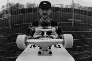 Black and white portrait of skateboarder Tobias Lehne holding his skateboard into the camera.