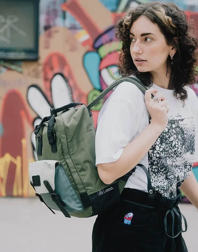 Young female model with curls wearing an olive-colored backpack over her right shoulder