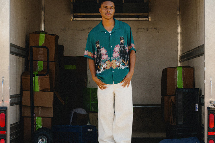 Portrait of a young male adult standing in an empty truck and wearing a green HUF button up with doberman dogs printed on.