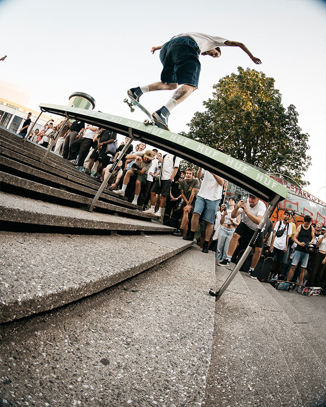 Photo of Jelle Maatman doing a Frontside Nosegrind down a gnarly handrail with a green topper during the HUF “Rail around the corner” event at SKTWK 2023.
