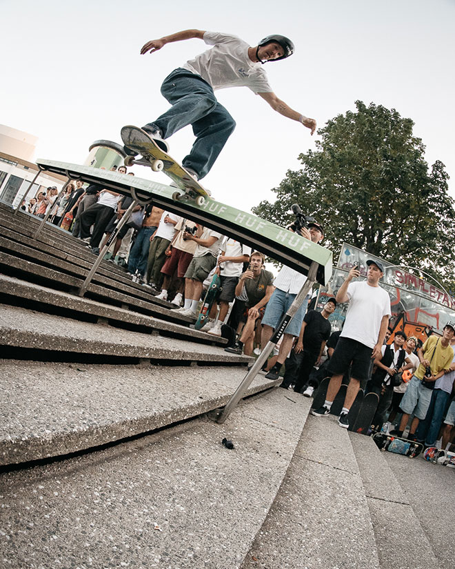 Photo of Alex Ullmann doing a Noseslide down a gnarly handrail with a green topper during the HUF “Rail around the corner” event at SKTWK 2023.