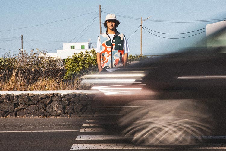 Portrait of a man standing in front of a pedestrian crossing, wearing a Parlez west with a colorful allover print, while a car is passing by.