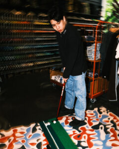 Portrait of a young male inside a streetwear shop, playing a mini golf tournament.