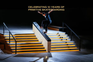 Photography of professional athlete Paul Rodriguez in his very own Primitive Skatepark, performing a Switch Bluntslide down a hubba ledge in a dark and ambient atmosphere. A golden typeface says »Celebrating 10 Years of Primitive Skateboarding«.
